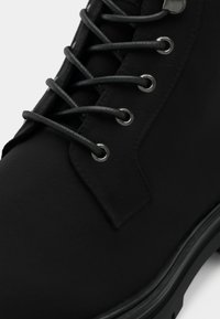 Černé kožené kotníkové boty s kulatou špičkou, texturovaným svrškem, šedými tkaničkami, metalickými očka a silnou černou gumovou podrážkou.