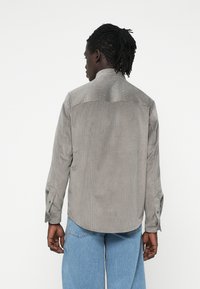 Camisa de pana gris con cuello, mangas largas y puños abotonados. Presenta una textura acanalada vertical y un dobladillo curvado.