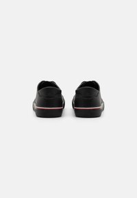 Zapatillas de cuero negro vistas desde atrás, con un acento de rayas rojas y blancas en la suela negra y una textura suave.