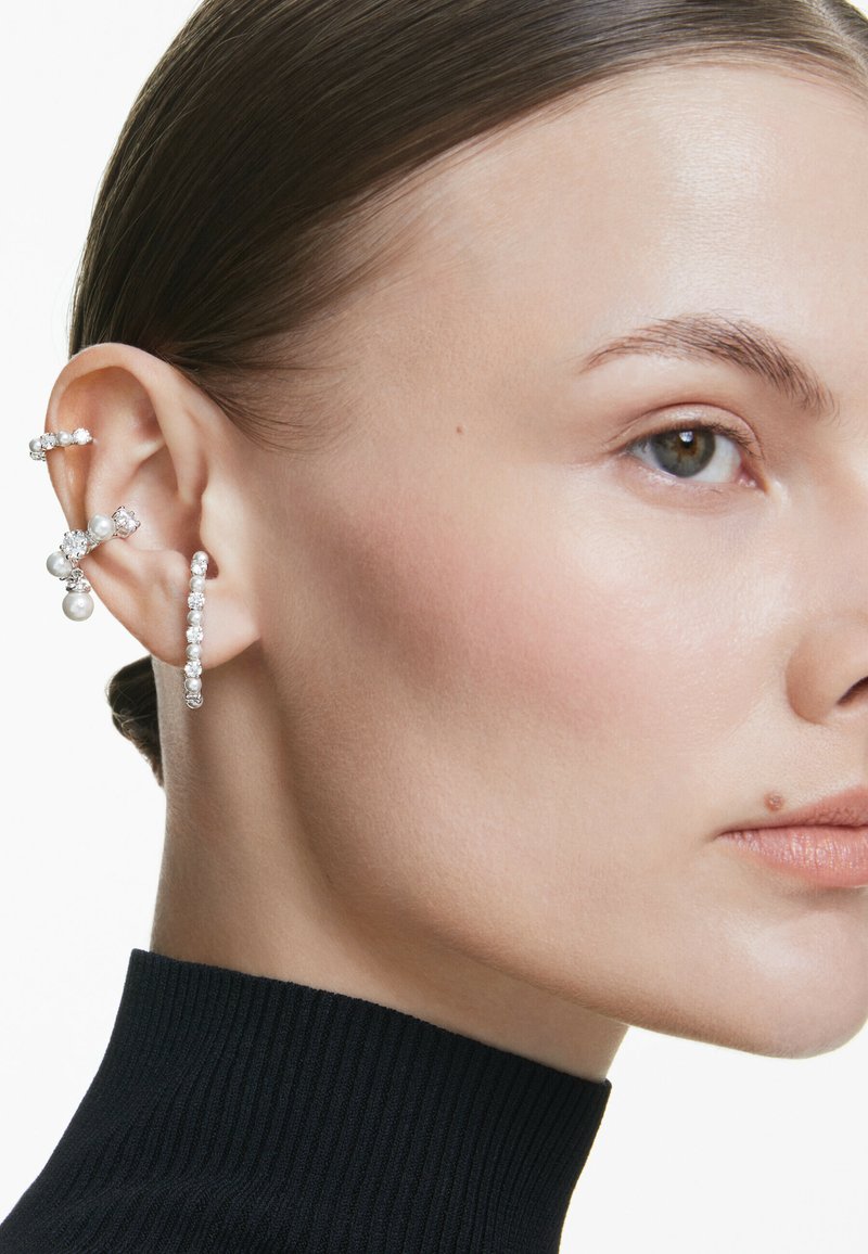 Súprava strieborných a perlových náušníc, ktorá obsahuje rôzne dizajny: kruhové, puzety a dekoratívne prvky, s trblietavými akcentmi a hladkým povrchom.