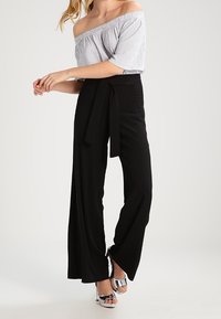 Schulterfreies gestreiftes Oberteil und hochtaillierte schwarze weite Hose mit gebundenem Gürtel, kombiniert mit glänzenden silbernen High Heels. Geschmeidige, fließende Stoffe.