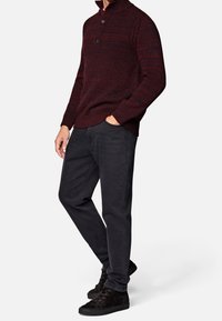 Pull-over tricoté bordeaux avec col haut et fermeture à deux boutons, associé à un jean noir et des chaussures noires à lacets. Texture douce, design décontracté.