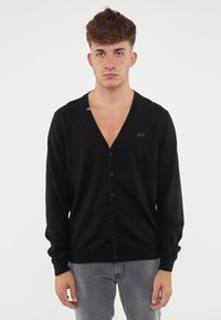 Cardigan nero con scollo a V e chiusura con bottoni. Maniche lunghe, texture morbida e un piccolo logo sul petto.