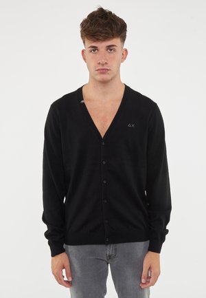 Cardigan nero con scollo a V e chiusura con bottoni. Maniche lunghe, texture morbida e un piccolo logo sul petto.