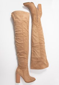 Stivali beige in suede, alti fino al ginocchio, con un ampio risvolto, tacco a colonna alto e dettaglio con zip laterale, caratterizzati da una texture liscia e punta arrotondata.