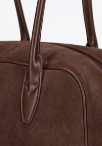 Bolso de ante sintético marrón con acentos de piel suave, que presenta asas dobles y un cierre con cremallera, mostrando una elegante forma rectangular.