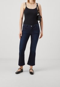 Černý tílko v kombinaci s tmavě modrými rozšířenými džíny. Džíny mají mírně pružný materiál, přední kapsy a pas s kovovým knoflíkem.