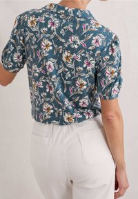 Camicia a maniche corte con colletto in teal con motivo floreale, caratterizzata da fiori bianchi, rosa e arancioni. Tessuto morbido con una vestibilità leggermente rilassata.