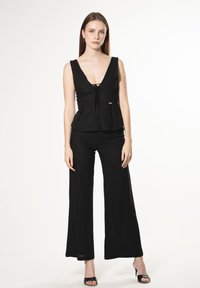 Top nero senza maniche con scollatura a V e dettaglio a fiocco, abbinato a pantaloni neri lunghi fino al pavimento. Tessuto leggero con una consistenza liscia.