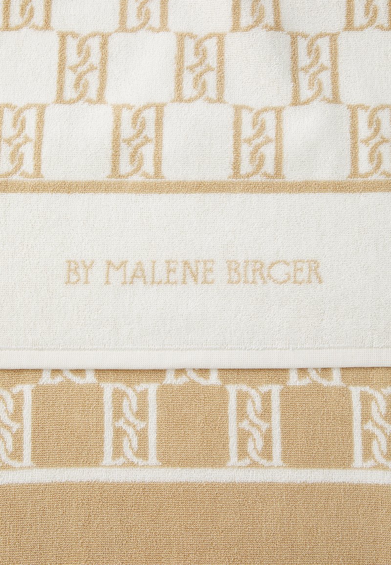 Asciugamano con un motivo geometrico in crema e beige chiaro, realizzato in tessuto testurizzato. "BY MALENE BIRGER" è impresso sulla fascia bianca.