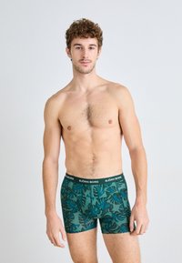 Grüne Boxershorts mit Muster und dunklen Blattdesigns sowie einem schwarzen Bund, auf dem "BJÖRN BORG" in weißem Text steht.