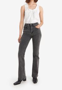 Jeans gris taille haute en denim, dotés de poches avant et d'une jambe légèrement évasée, associés à un débardeur blanc à volants et des bottes noires.