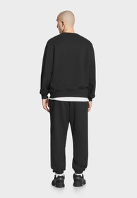 Czarna bluza i joggery z miękkiego materiału, z prążkowanymi mankietami i paskiem w talii, noszone z czarnymi sneakersami, widok z tyłu.
