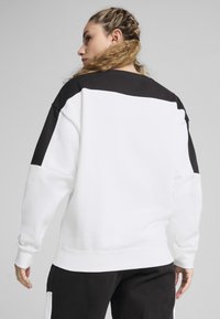 Valge sweatshirt mustade õlgade ja seljaosalaga. Omab pikki varrukaid, soonikkoes mansette ning vabalt langevat lõiget. Sile kangast tekstuur.