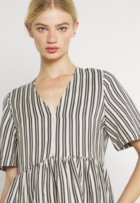 Gestreiftes Kleid in Beige und Schwarz, mit V-Ausschnitt, kurzen Ärmeln und gerafftem Bund für einen lockeren Sitz, aus leichtem Stoff gefertigt.