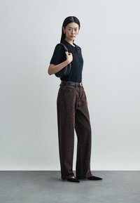 Black fuzzy short-sleeve top, dark brown patterned wide-leg pants, black belt with gold buckle, and black handbag. Black pointed-toe shoes.