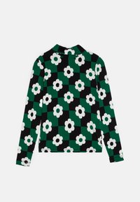 Langermet topp med et svart og grønt rutemønster og hvite blomster. Laget av elastisk stoff med krage.