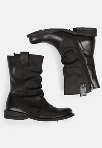 Botas de tobillo de cuero negro con un diseño arrugado, cremallera lateral y suela de goma texturizada. Presentan costuras sutiles y un tacón plano.