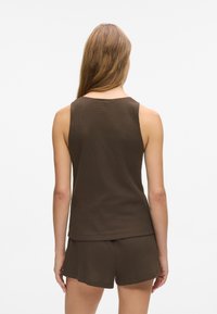 Top de culoare maro, cu model ribat, purtat împreună cu pantaloni scurți asortați. Dispune de un decolteu rotund și o croială lejeră, realizat dintr-un material moale, texturat.