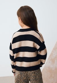 Brun og sort stribet strikket sweater med ribbet tekstur. Bruges med beige og brune leopardprintbukser. Set bagfra, afslappet pasform.