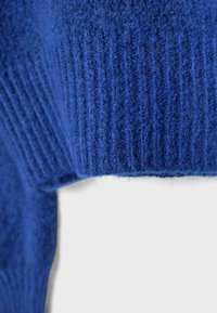 Pletený sveter v tmavomodrej farbe, s rebrovanou textúrou a jemným, chlpatým materiálom. Golier a lem majú jednotné, pevné rebrovanie.