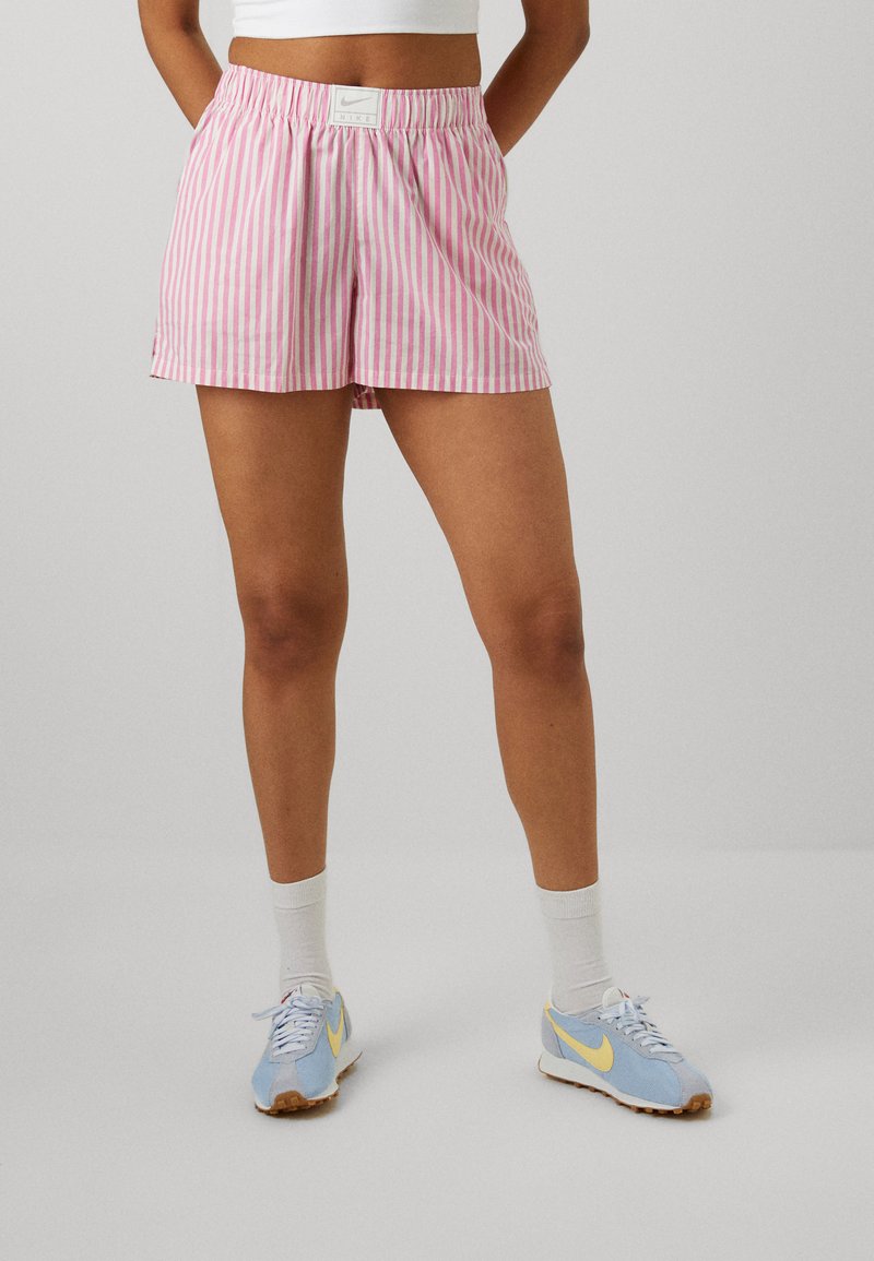 Shorts rayés rose et blanc en tissu léger, dotés d'une taille élastique. Associés à des baskets Nike bleu clair et des chaussettes blanches.