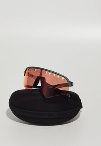 Sonnenbrille mit rahmen in Türkis und roten Gläsern, ausgestattet mit Belüftungslöchern und einem schwarzen Hartschalenetui zur Aufbewahrung.