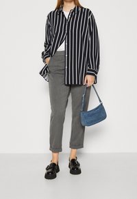 Gestreiftes Hemd in Marineblau und Weiß, graue Hose, schwarze Plateauschuhe und eine kleine blaue Jeanshandtasche.