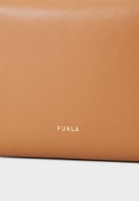 Lærveske i tan-farge med teksturert overflate, med et gull-logo. Minimalistisk design, rektangulær form og glatte kanter.