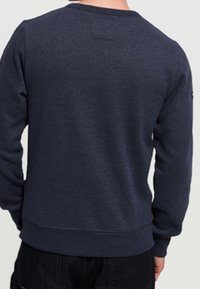 Felpa blu navy con collo a giro e polsini a costine. Realizzata in tessuto con una texture morbida. Nessun logo visibile sul retro.