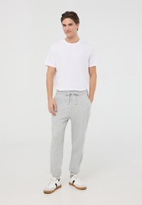 Pantaloni jogger grigi in cotone con vita elasticizzata e coulisse. Abbinati a una t-shirt bianca a maniche corte e sneakers bianche con dettagli neri.