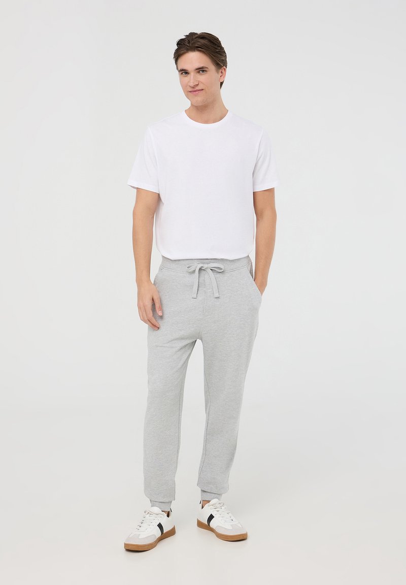 Pantaloni jogger grigi in cotone con vita elasticizzata e coulisse. Abbinati a una t-shirt bianca a maniche corte e sneakers bianche con dettagli neri.