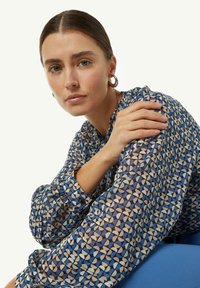 Blauwe blouse met een patroon van abstracte vormen, gemaakt van lichtgewicht stof. Heeft lange mouwen en een ronde halslijn.
