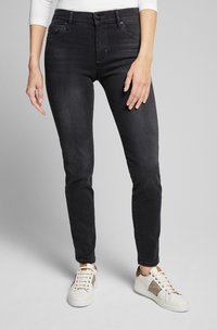 Schwarze Denim-Jeans mit Slim-Fit, ausgestattet mit vorderen Taschen, Gürtelschlaufen und einem Knopfverschluss. Kombiniert mit weißen Sneakers und einem hellen Oberteil.