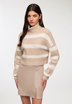 Maglione a strisce beige, tagliato, con collo a maniche lunghe e a costine, abbinato a una gonna beige al ginocchio con una fessura laterale.