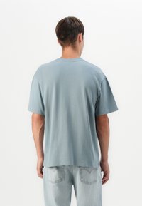 Világoskék pamut póló kerek nyakkal és rövid ujjakkal, laza szabással és puha tapintással. Hátulról nézve a design egyszerűségét mutatja.