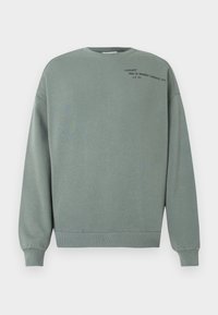 Sudadera verde polvorienta con mangas largas y pequeño texto negro que dice "Carhartt Work In Progress (Detroit) 1989 A.C 313" en la parte superior izquierda del pecho.