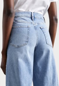 Jeans de tiro alto en azul claro con un diseño de pierna recta, que cuentan con dos bolsillos traseros y detalles de costura sutiles.