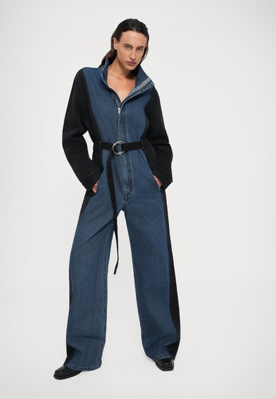 Salopette in denim blu e nera, con colletto alto, maniche lunghe, vita aderente con cintura e pantaloni a gamba larga.