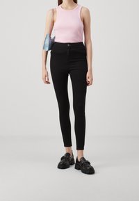 Jeans ajustados de tiro alto en negro combinados con una camiseta sin mangas de canalé en rosa claro y zapatos de plataforma negros gruesos con detalles de tachuelas.