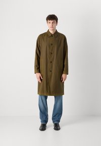 Olive green raincoat with a button closure, featuring a collar, two front pockets, and a straight fit, paired with light blue jeans.
