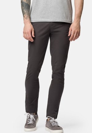 Szare spodnie slim-fit wykonane z lekkiego, elastycznego materiału, z bocznymi kieszeniami i gładkim wykończeniem, zestawione z szarymi trampkami.