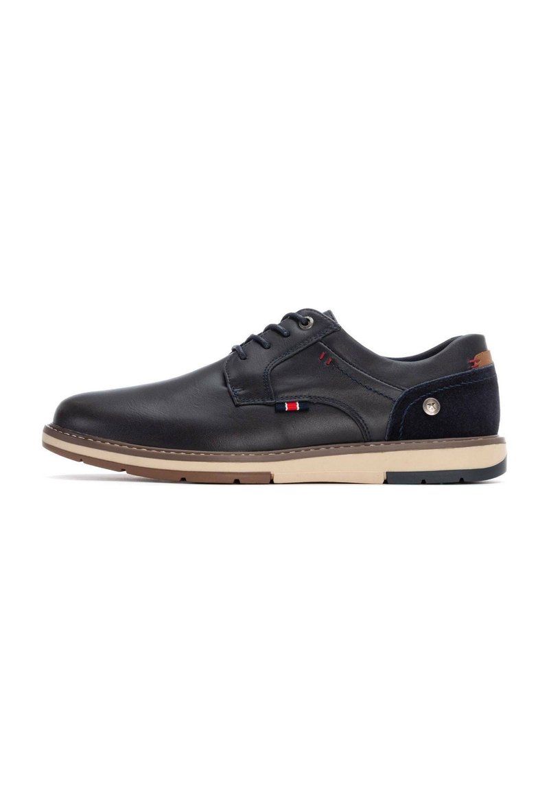 Zapatos de cuero negro con textura suave, perfil bajo, suela beige, acentos azules y un pequeño logotipo en el costado. Presentan un clásico diseño de cordones.