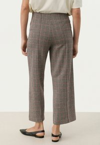 Šedé kostkované kalhoty s širokým střihem, se červenými a černými akcenty, vysokým pasem a hladkou texturou. Nosené s černými slingback botami.