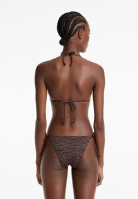 Bikini set s potiskem zebry v černé a hnědé barvě, s uvazováním na krku a po stranách, vyrobený z texturované tkaniny a s minimálním krytím.