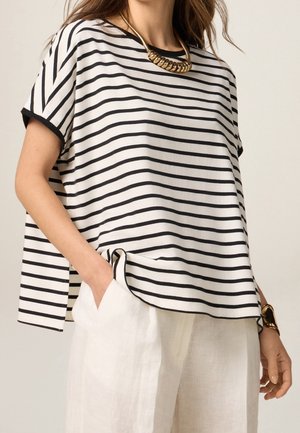 Zwart-wit gestreept topje met korte mouwen en een losse pasvorm, met een ronde halslijn en een gouden ketting. Gecombineerd met lichte linnen broek.