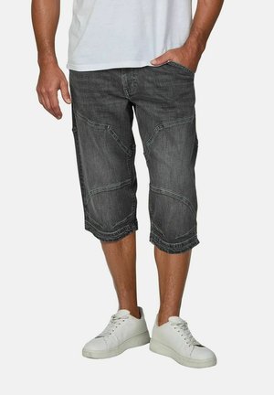 Zwarte denim capri-broek met een losse pasvorm, voorzien van hoekige stiksel details en opgerolde zomen, gecombineerd met witte sneakers.