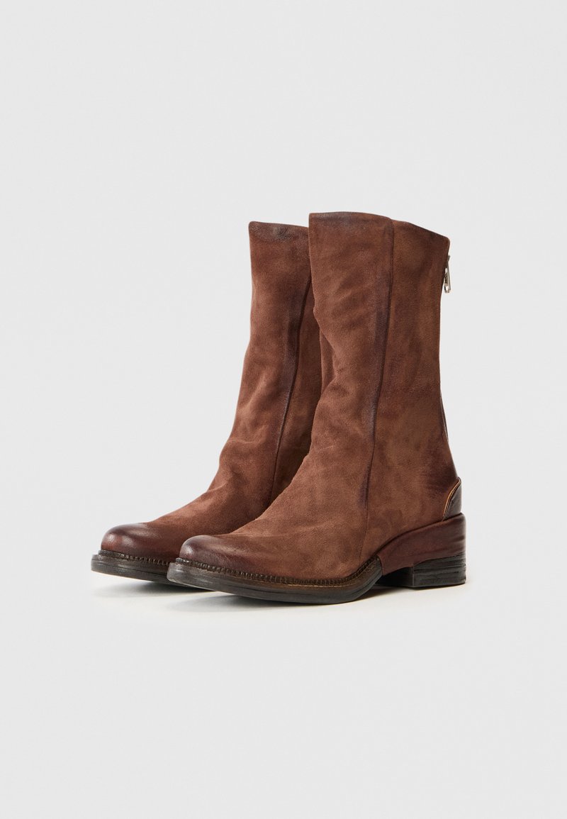 Une paire de bottes en suède marron mi-mollet avec des talons bas empilés et des bouts ronds, mettant en avant des zips sur le côté et une finition lisse sur fond blanc.