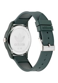 Montre avec bracelet en silicone vert et fond de boîtier en acier inoxydable, avec une bande texturée, un logo gravé et un fermoir en métal sécurisé.
