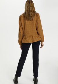 Blusa marrone a maniche lunghe con motivo a quadri e orlo a peplo. Abbinata a jeans skinny blu scuro e stivaletti neri. Tessuto liscio, design casual.